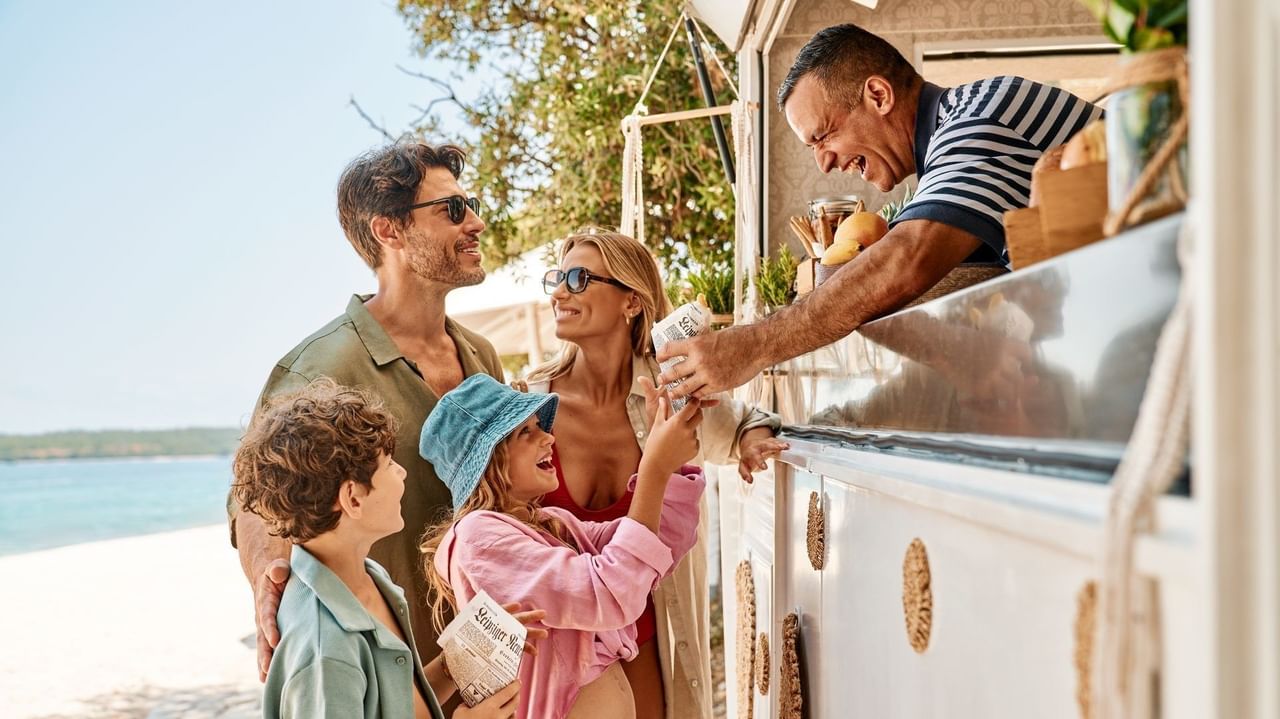 Familie kauft von einem mobilen Essensstand an einem Strand an einem sonnigen Tag.