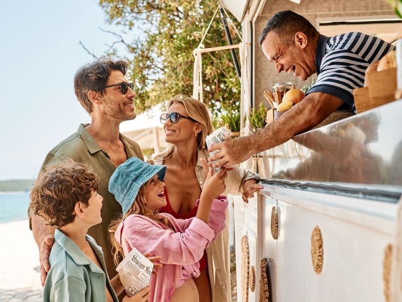 Famiglia felice compra cibo da un camioncino vicino alla spiaggia.