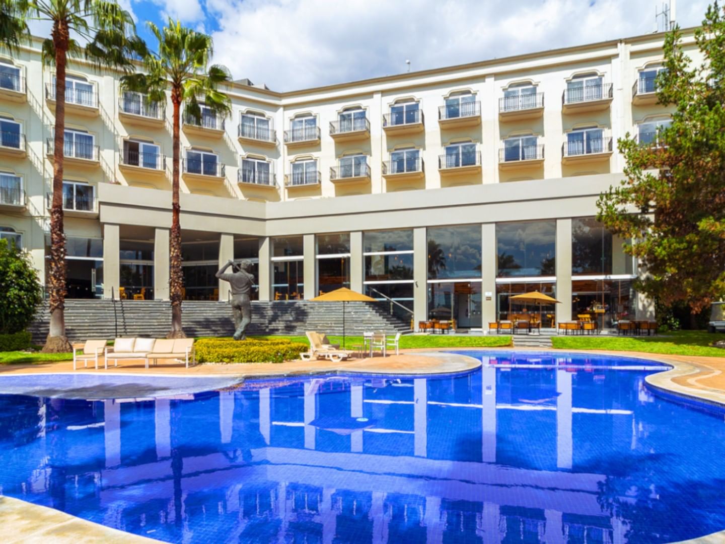 Large outdoor swimming pool and hotel facade with palm trees on-site at Camino Real Pedregal Mexico