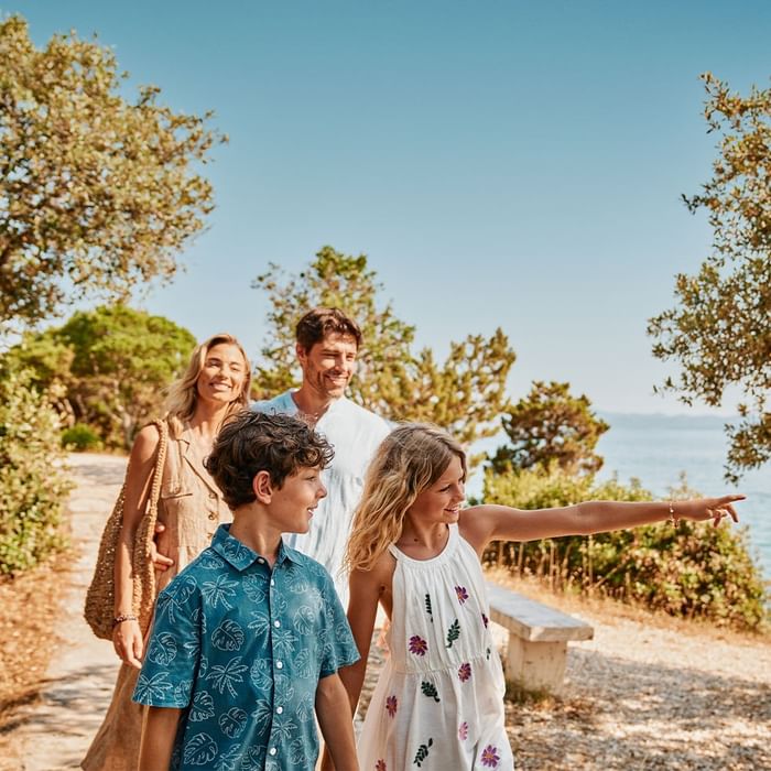 Family strolls by beachside path with greenery and sea view at Falkensteiner Resort Lake Garda