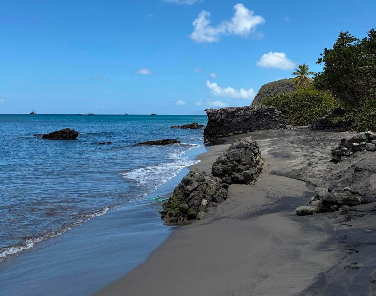 Waves gently washing onto a dark volcanic sand beach with rocky stone formations at Golden Rock Resort