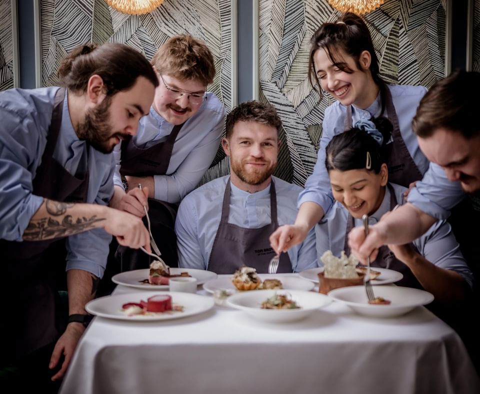 Chefs plating dishes by gold wall lamps at a dining table in The Capital Hotel, Apartments and Townhouse