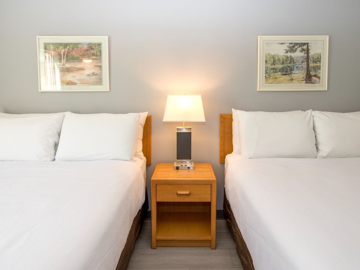 Two twin beds with white bedding, a nightstand with a lamp, and two framed pictures on the wall.