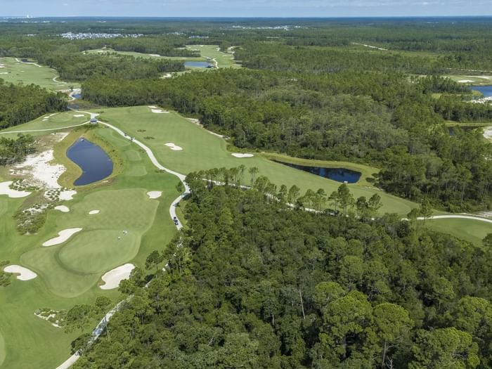 Aerial view of The Third golf course in Panama City Beach, Florida, with ponds, sand traps, and dense trees, set against a clear sky.