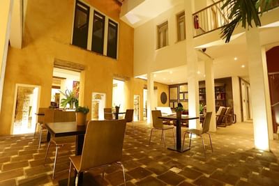 Illuminated courtyard with wooden tables and chairs, surrounded by yellow walls and greenery at Billini Hotel Historic Luxury