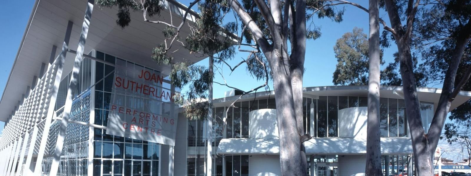 Joan Sutherland Performing Arts Centre building with large glass windows and trees in front under a clear blue sky.