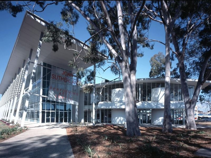 Joan Sutherland Performing Arts Centre building with large glass windows and trees in front under a clear blue sky.