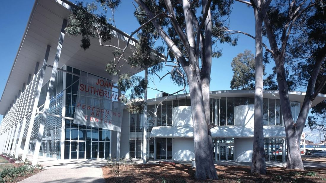 Modern building named Joan Sutherland Performing Arts Centre with glass facade and large trees in front.