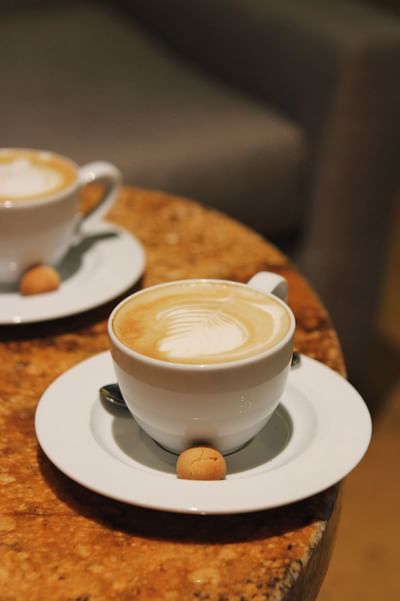 Dos tazas de café con leche y galletas en platos blancos sobre una mesa.