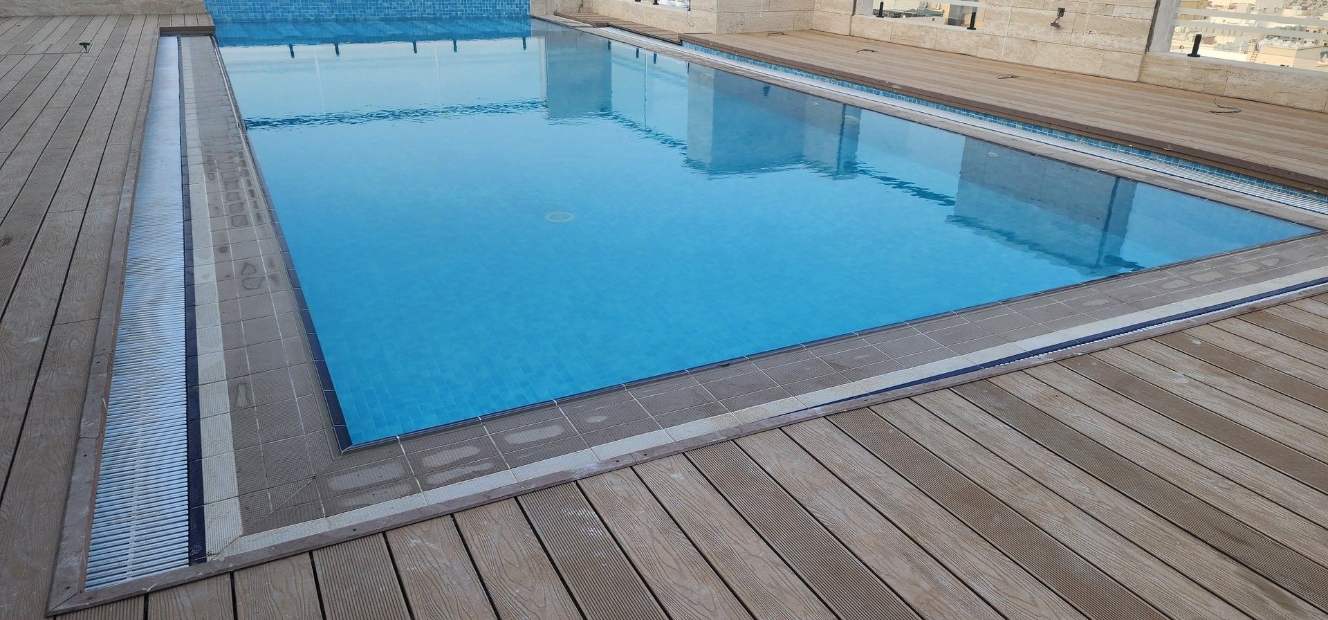Outdoor pool with blue water surrounded by a wooden deck and light stone walls at Warwick Jeddh Hotel & Spa