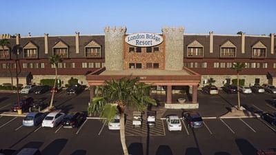 Front exterior view of castle-themed hotel building with stone towers and parking lot at London Bridge Resort