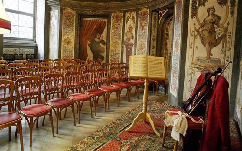 Historic concert room in Mozarthaus Vienna with classical chairs, decorative wall paintings and a music stand with a violin.