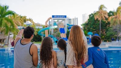 Family of five viewing colorful water slides and pool area surrounded by palm trees at Playa Blanca Beach Resort NEW SITE