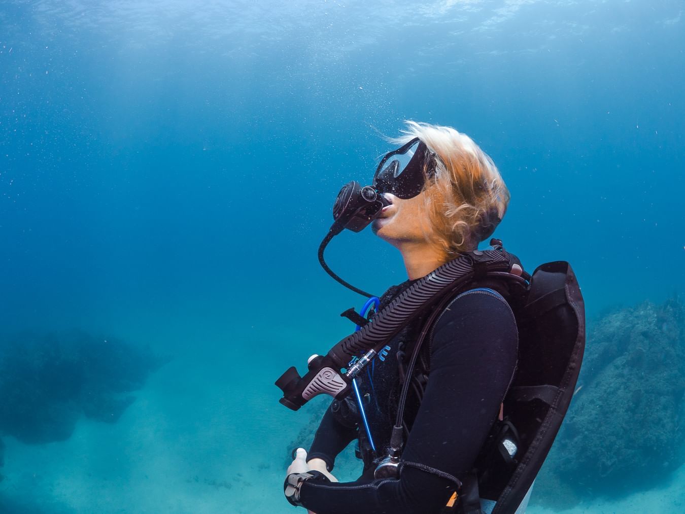 Scuba diver in full diving gear, equipped with an oxygen mask, underwater near the deep ocean at Golden Rock Resort