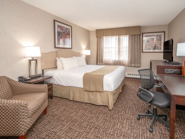 A hotel room with a bed, chair, desk, TV, and window with curtains.