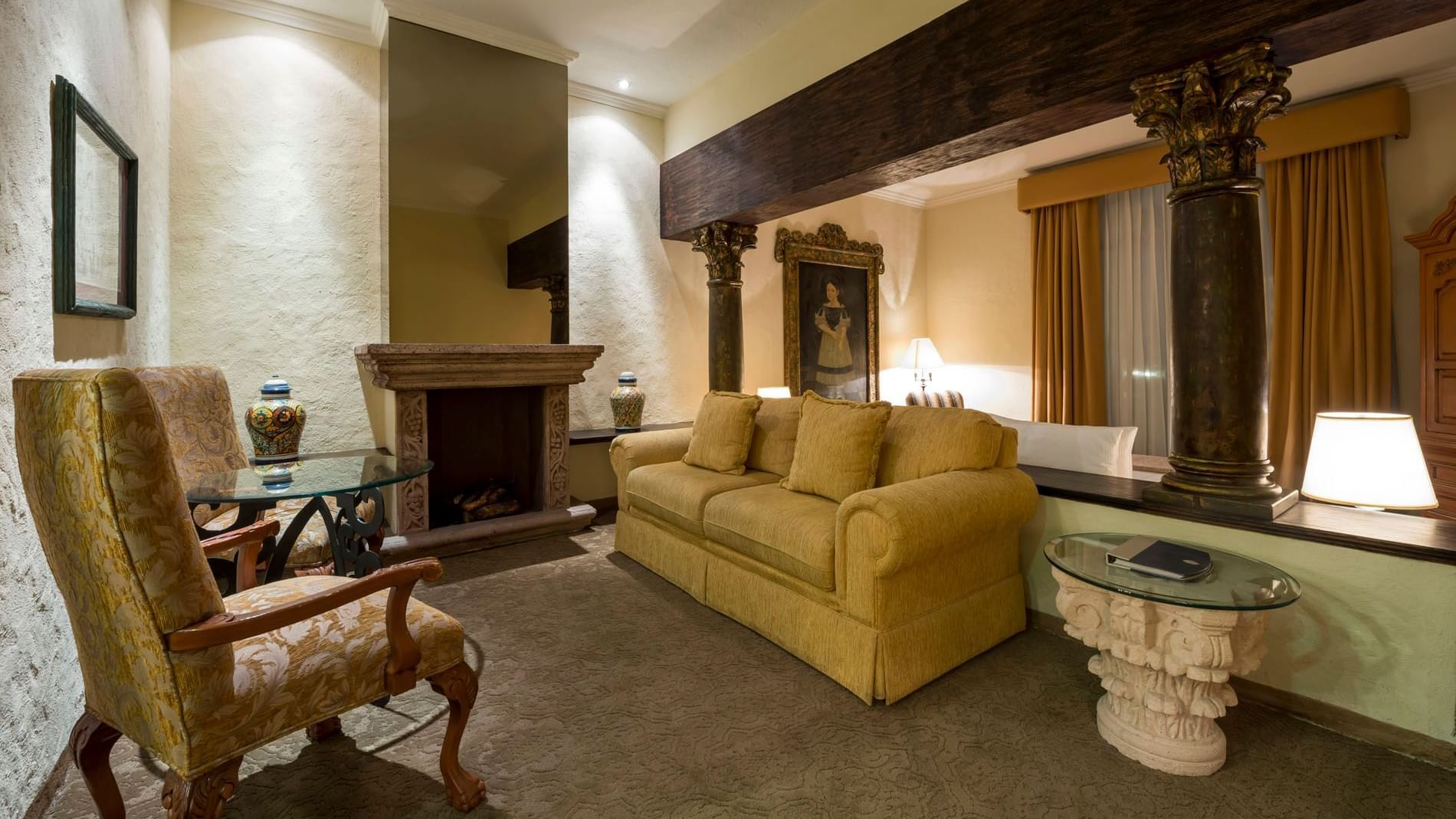 King Grand Class Sitting area with a fireplace, yellow sofa, and stone columns at the grand Quinta Real Aguascalientes