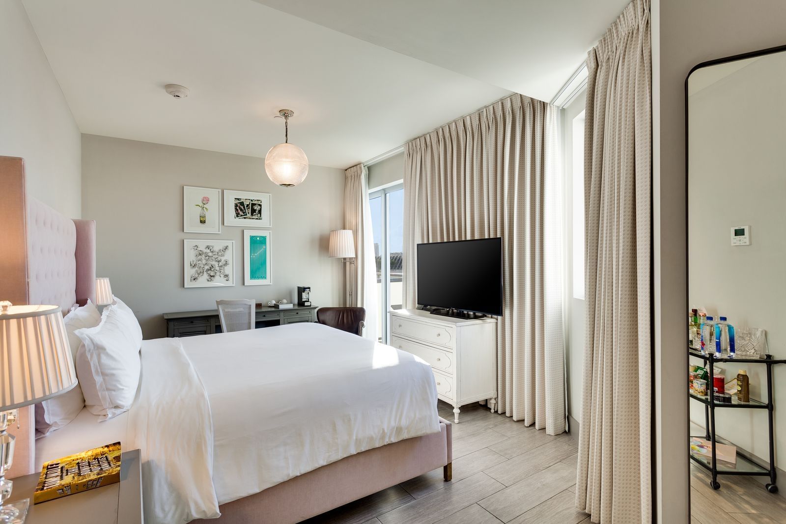 A wide view of a hotel suite with a large bed, flat-screen TV, and bar cart.
