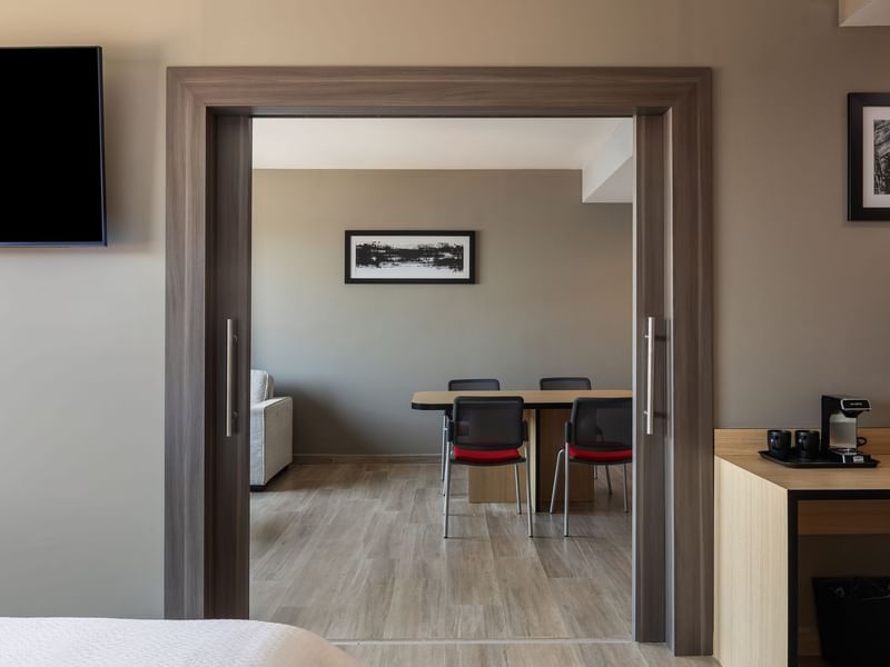 Junior suite king at Gamma Hotels with a king bed, sofa, wooden dining table with chairs, TV, and a coffee station