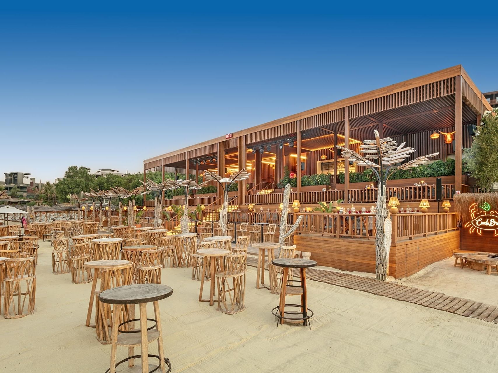 Chic open-air bar on sandy ground at Titanic Luxury Collection Bodrum, lined with stylish tables.