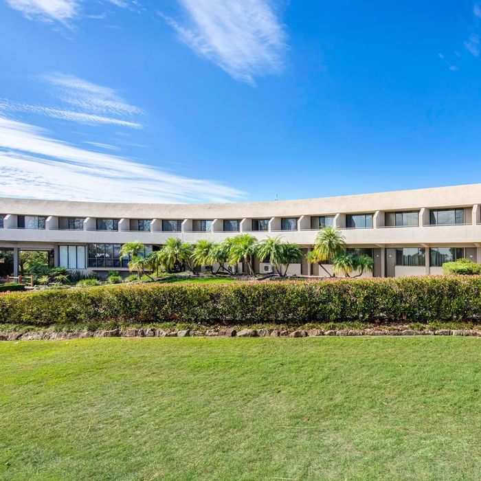 View of the garden & hotel exterior surrounded by lush greenery & palm trees, under a clear blue sky at Mercure Charlestown