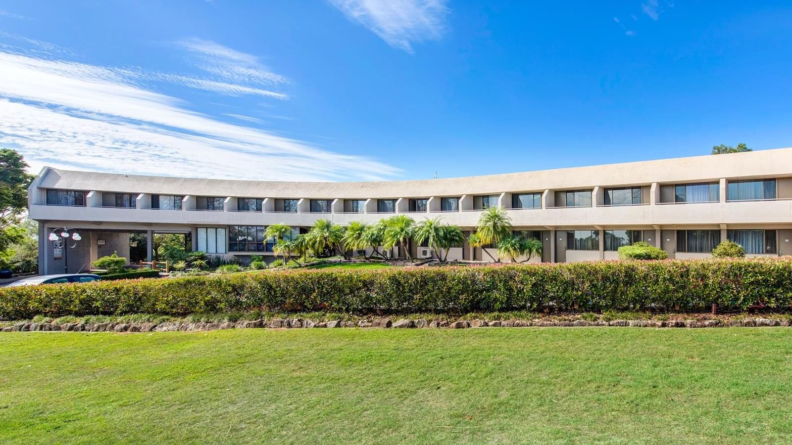 View of the garden & hotel exterior surrounded by lush greenery & palm trees, under a clear blue sky at Mercure Charlestown