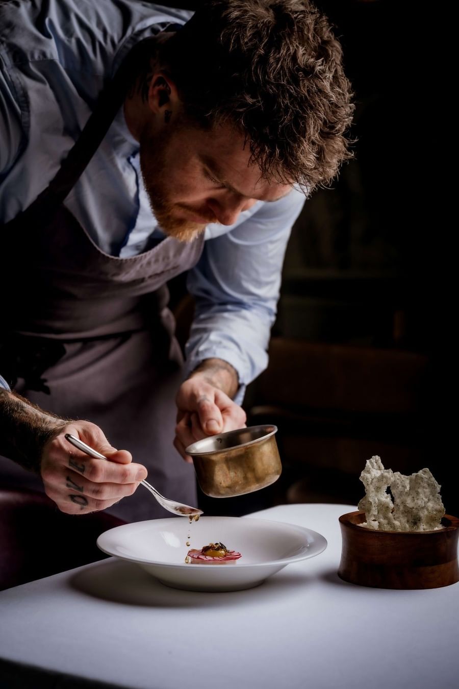 Chef in an apron holding a metal pot and spoon while plating food at The Capital Hotel, Apartments and Townhouse