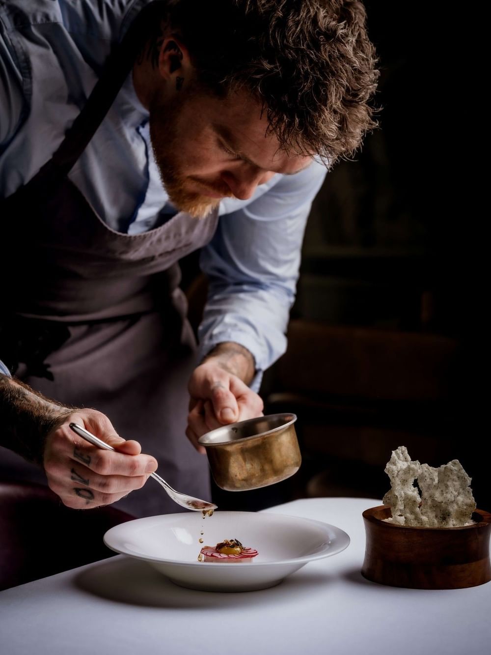 Chef in an apron holding a metal pot and spoon while plating food at The Capital Hotel, Apartments and Townhouse