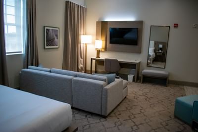 Deluxe King Grand living area with a gray sectional couch, TV mounted over a desk, and a mirror at Centennial Plaza Resort