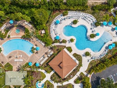 Aerial view of the Vista Cay Resort with two pools, lounge chairs, umbrellas, and tropical surroundings.