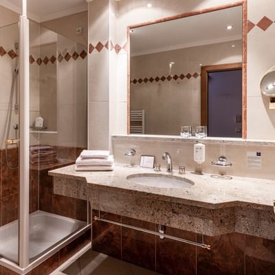 Bagno elegante con doccia e servizi nella Garden Family Room al Falkensteiner Hotel Falkensteinerhof a Valles.