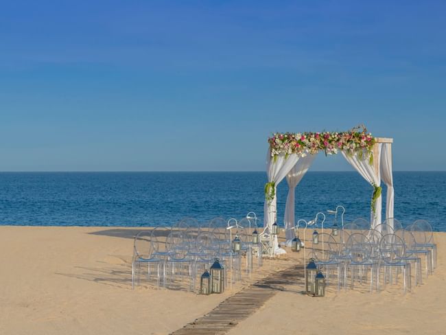A romantic beach ceremony setup at Hacienda del Mar Los Cabos with a floral arch and clear chairs