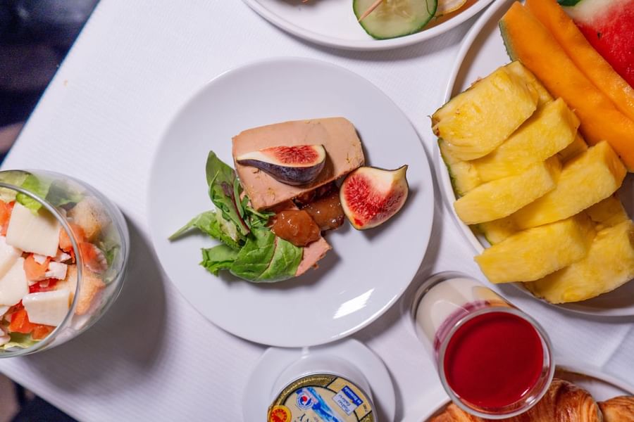Assortiment de mets pour le petit-déjeuner servis dans des assiettes, accompagnés d’un verre de jus de fruits et d’une pièce maîtresse composée de foie gras garni de figues, au Warwick Paris Champs-Élysées