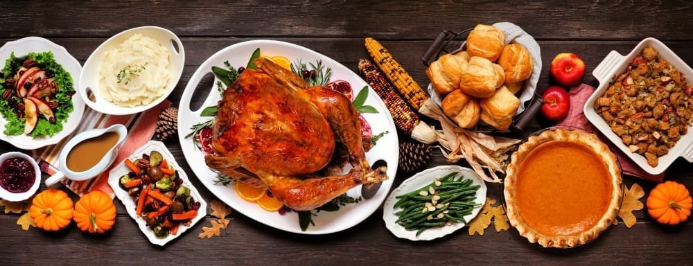 An aerial view of a Thanksgiving table spread, with a turkey, maize, pumpkin pie, side dishes, and pumpkins.