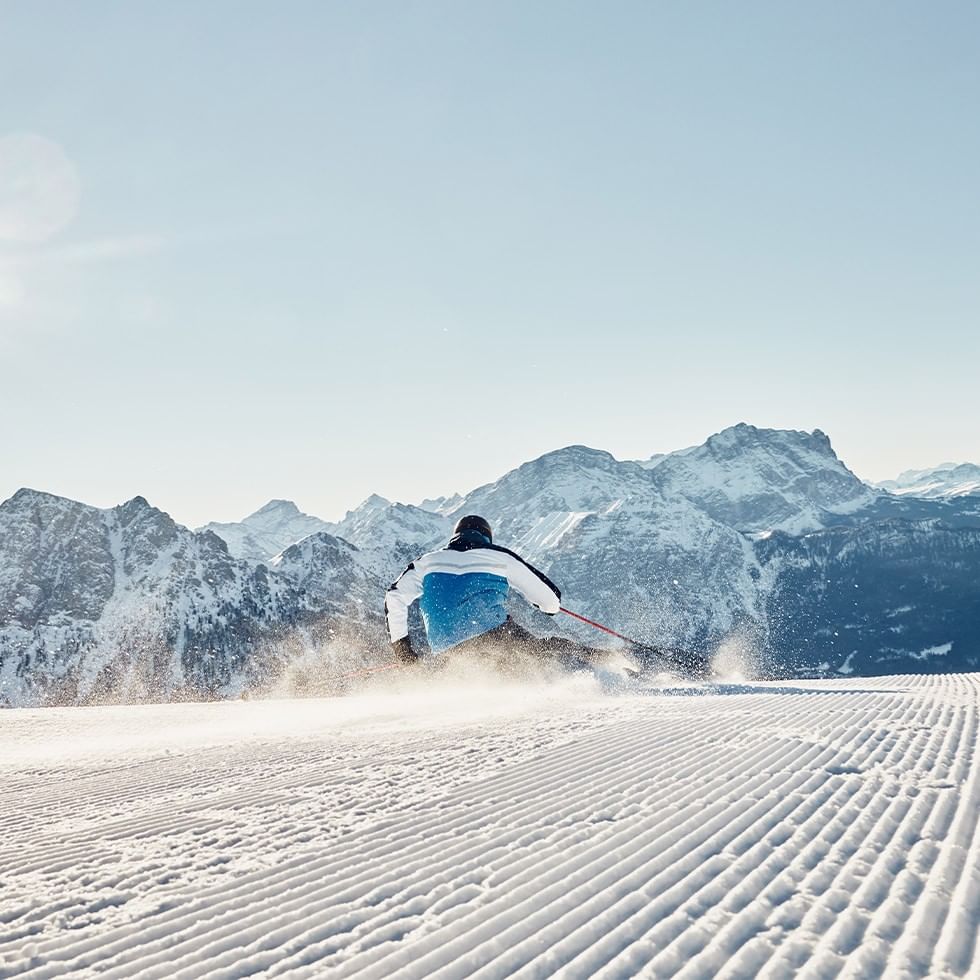 Sciatore in discesa sulle Alpi con montagne innevate sullo sfondo.