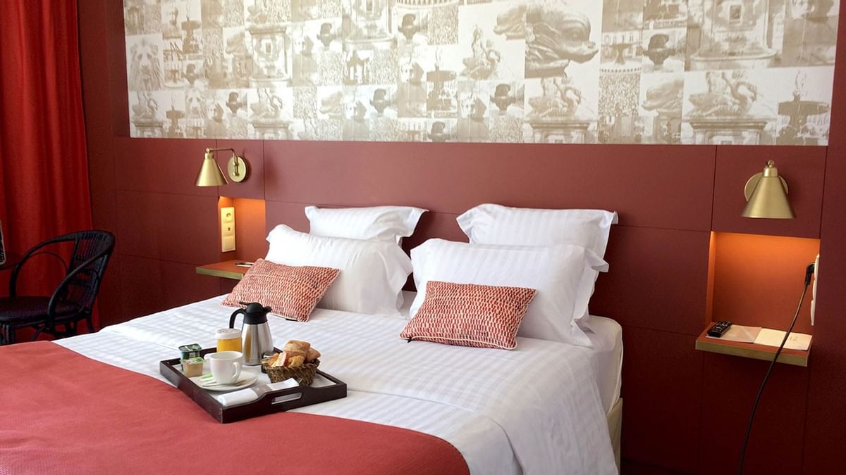 Chambre d'hôtel avec lit, mur décoré, plateau de petit-déjeuner, et chaise en arrière-plan.