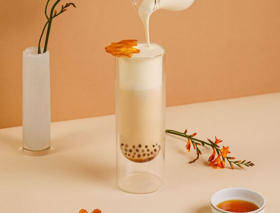 Hand pouring creamy milk over a glass of bubble tea served in Park Lounge at Park Hyatt Saigon