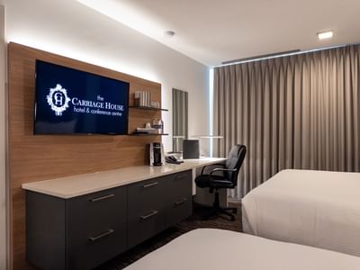 Modern hotel room with desk, chair, TV, and two beds at Carriage House Hotel & Conference Centre