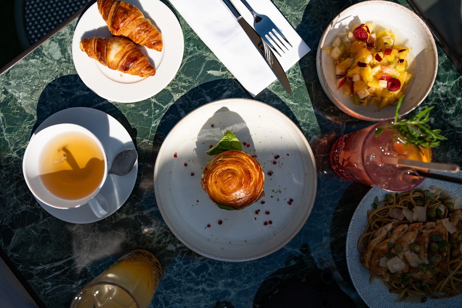 Breakfast dishes with croissants, tea and fruit by a pink drink on a marble table at Restaurant, Bar & Terrace Le W