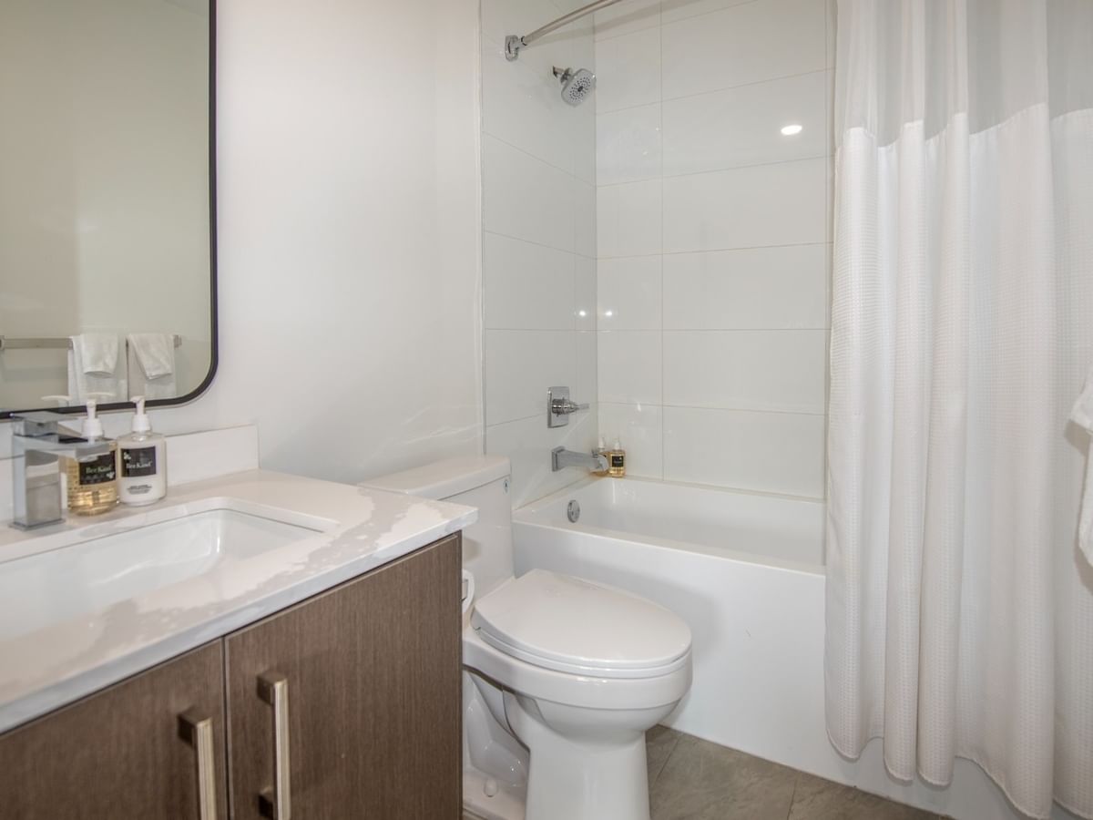 A modern bathroom with a white bathtub, toilet, sink, and mirror, plus a white shower curtain and towels.