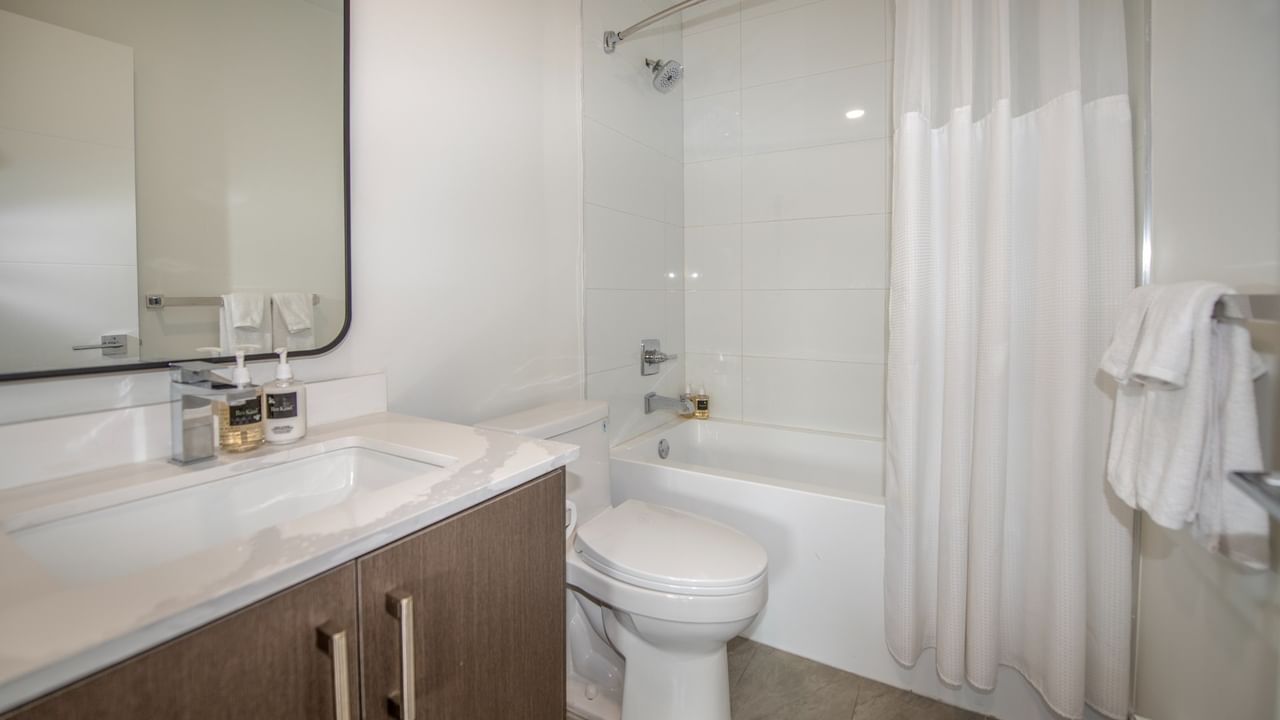 A modern bathroom with a white bathtub, toilet, sink, and mirror, plus a white shower curtain and towels.
