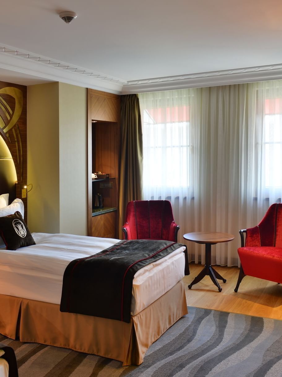 Single bed by a green desk under a red floor lamp surrounding a sitting area in Deluxe Rooms at Warwick Ankara