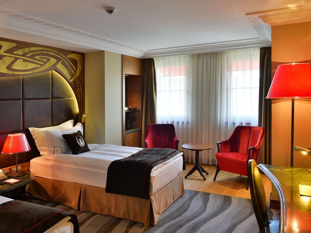 Single bed by a green desk under a red floor lamp surrounding a sitting area in Deluxe Rooms at Warwick Ankara
