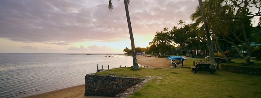 Green lawn by a stone wall near a sandy beach under a cloudy sunset sky near The Naviti Resort - Fiji