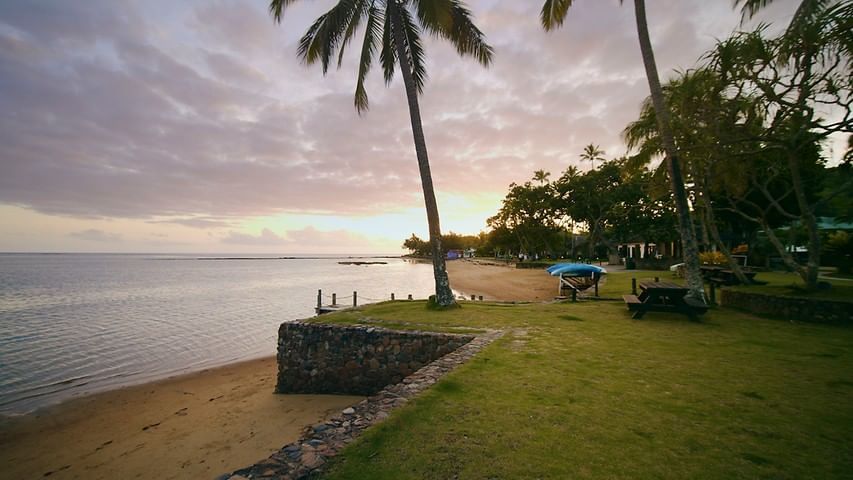 Green lawn by a stone wall near a sandy beach under a cloudy sunset sky near The Naviti Resort - Fiji
