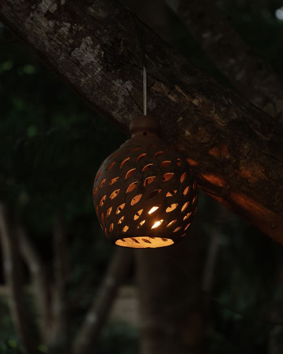 Handcrafted clay lantern glowing at night, hanging from a tree at Morgan\'s Rock, a Nicaragua sustainable hotel