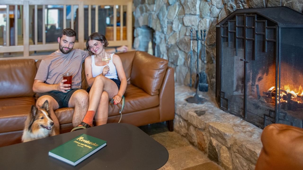 Couple sitting on a couch next to a fireplace with their pet