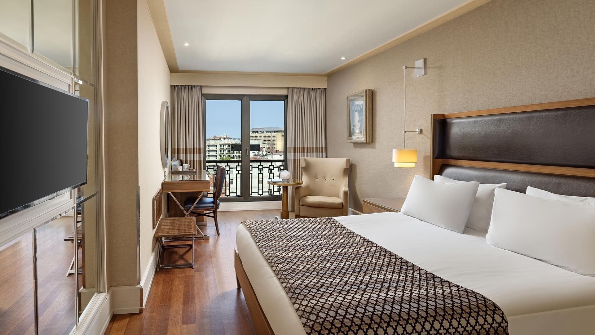Titanic City Taksim’deki Superior odada büyük yatak, balkon, masa, sandalye, televizyon ve dekorlu duvar.