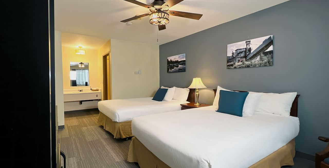 Hotel room with two beds, paintings, ceiling fan, mirror, night stand, and lamp