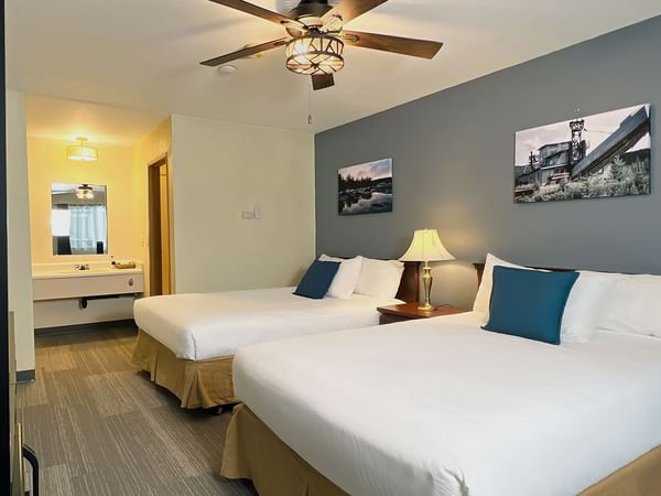 Hotel bedroom with two beds, lamp, ceiling fan, mirror, and paintings