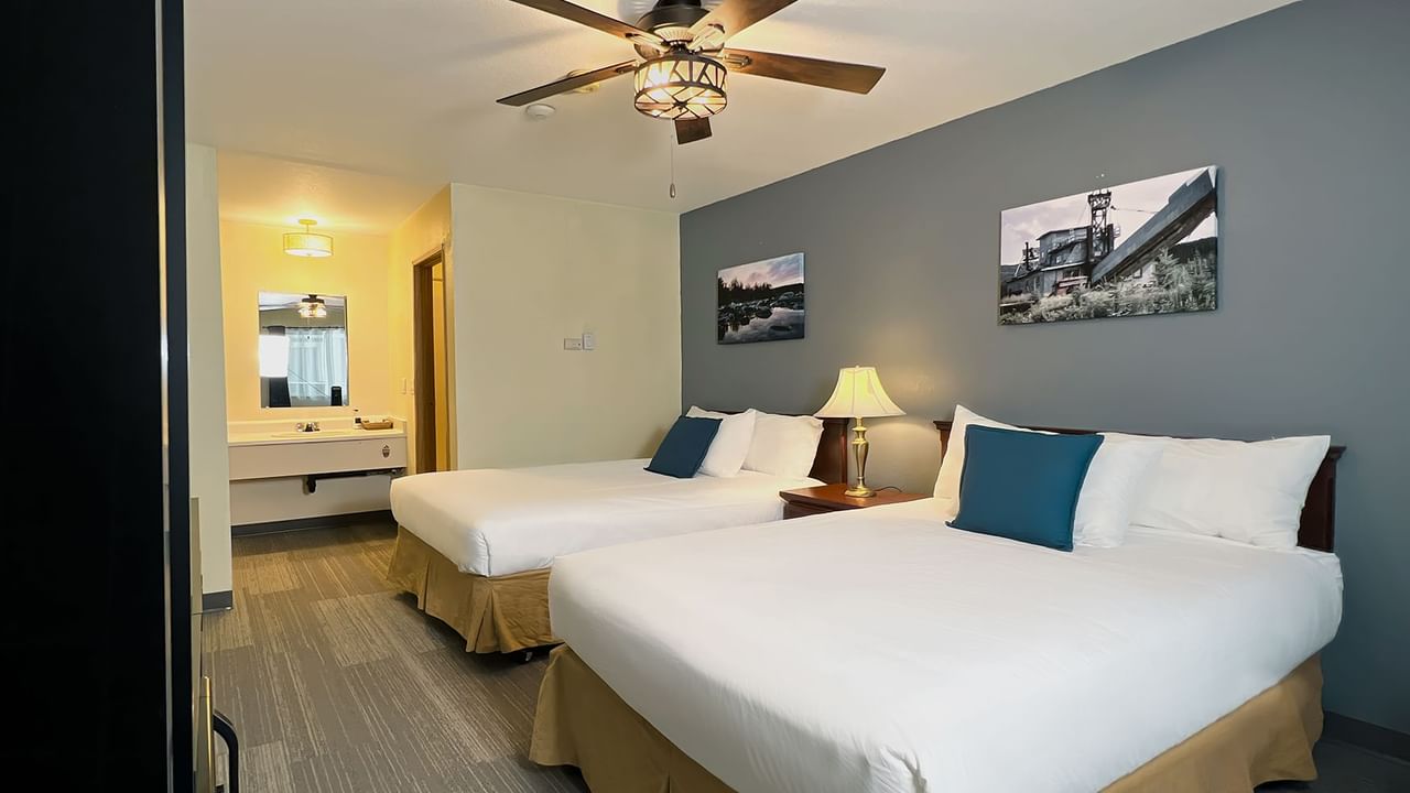 Hotel bedroom with two beds, lamp, ceiling fan, mirror, and paintings